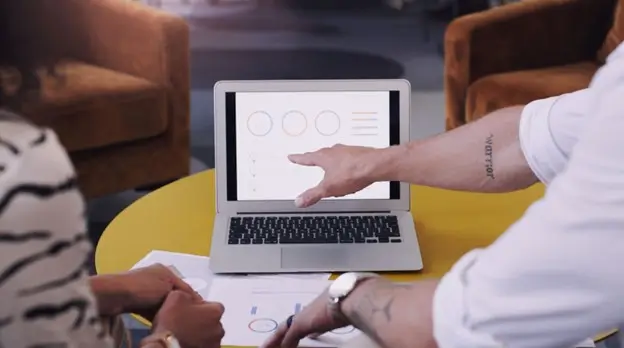 A man and woman sit together at a table, collaborating on a laptop, illustrating teamwork and shared effort.