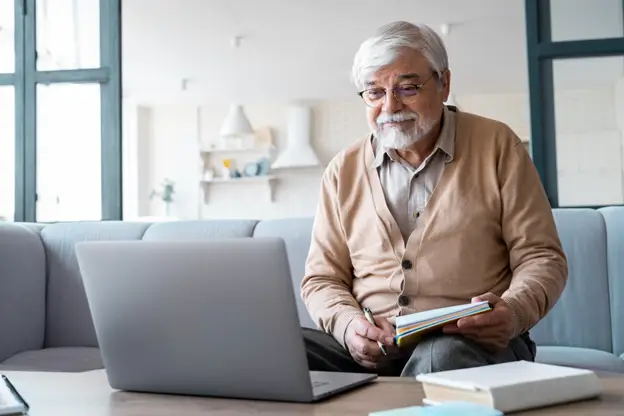 A senior man relaxing on a couch while working on a laptop, embodying a blend of comfort and productivity in his space.