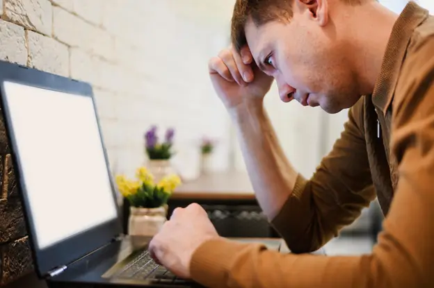 A man observes his laptop screen with concentration, engaged in work or research in a bright setting.