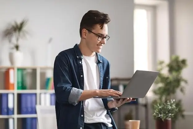 A man wearing glasses is focused on using a laptop, engaged in his work or study.