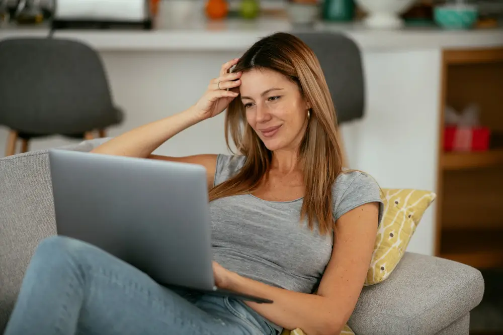 A woman seated on a couch, focused on her laptop, creating a cozy and productive home environment.