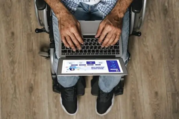 A man in a wheelchair is focused on using a laptop computer, showcasing accessibility and technology integration.