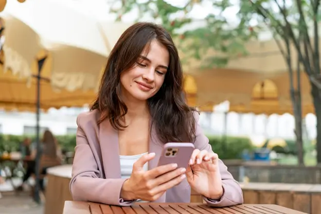 A woman seated at a table, focused on her phone, with a serene expression in a cozy environment.