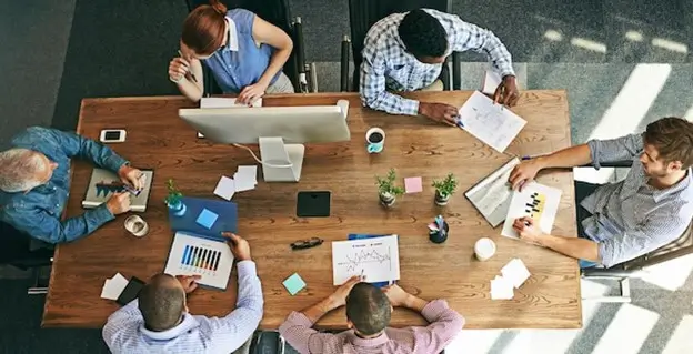 A diverse group of individuals engaged in discussion around a table covered with papers and documents.