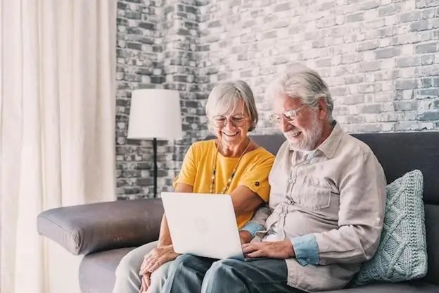 A senior couple on a couch, using a laptop, illustrating companionship and shared interests in a cozy setting.