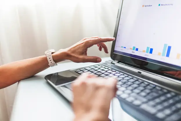 A person working on a laptop with graphs displayed on the screen.