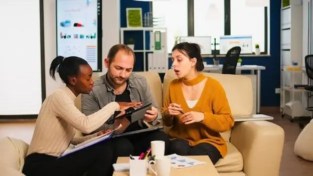 Three individuals seated on a couch in a modern office environment, engaged in conversation and collaboration.