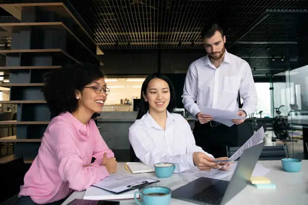 Three individuals sitting at a table, working on a laptop.