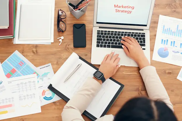 Woman typing on laptop with "Marketing Strategy" displayed on screen.