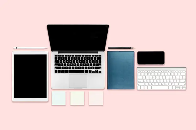 A laptop and phone alongside various items, all set against a vibrant pink background.