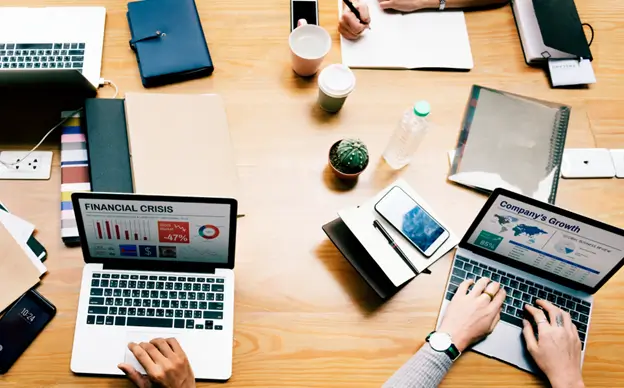 A team of workers gathered around a table, each using a laptop.