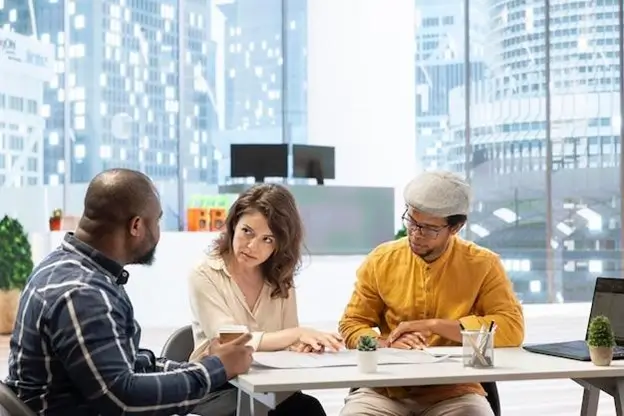 Three individuals seated at a table in an office setting, engaged in discussion or collaboration.